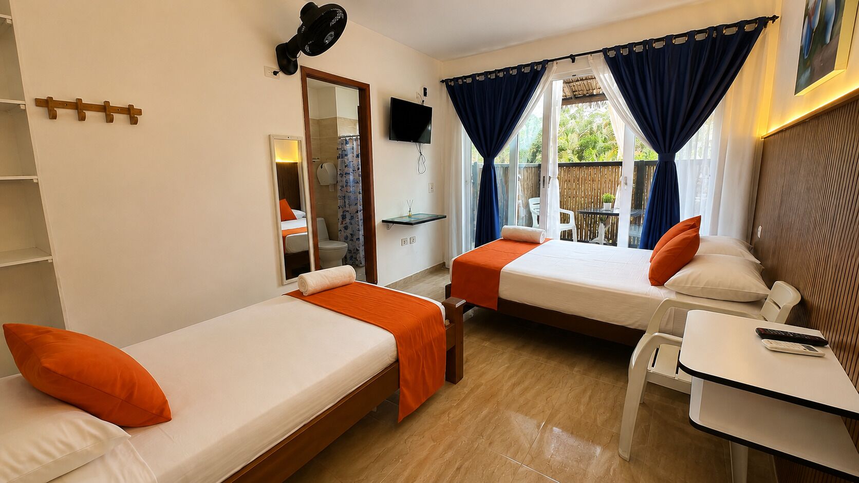 A room with two single beds, a desk, a chair, a TV, and a window with curtains.
