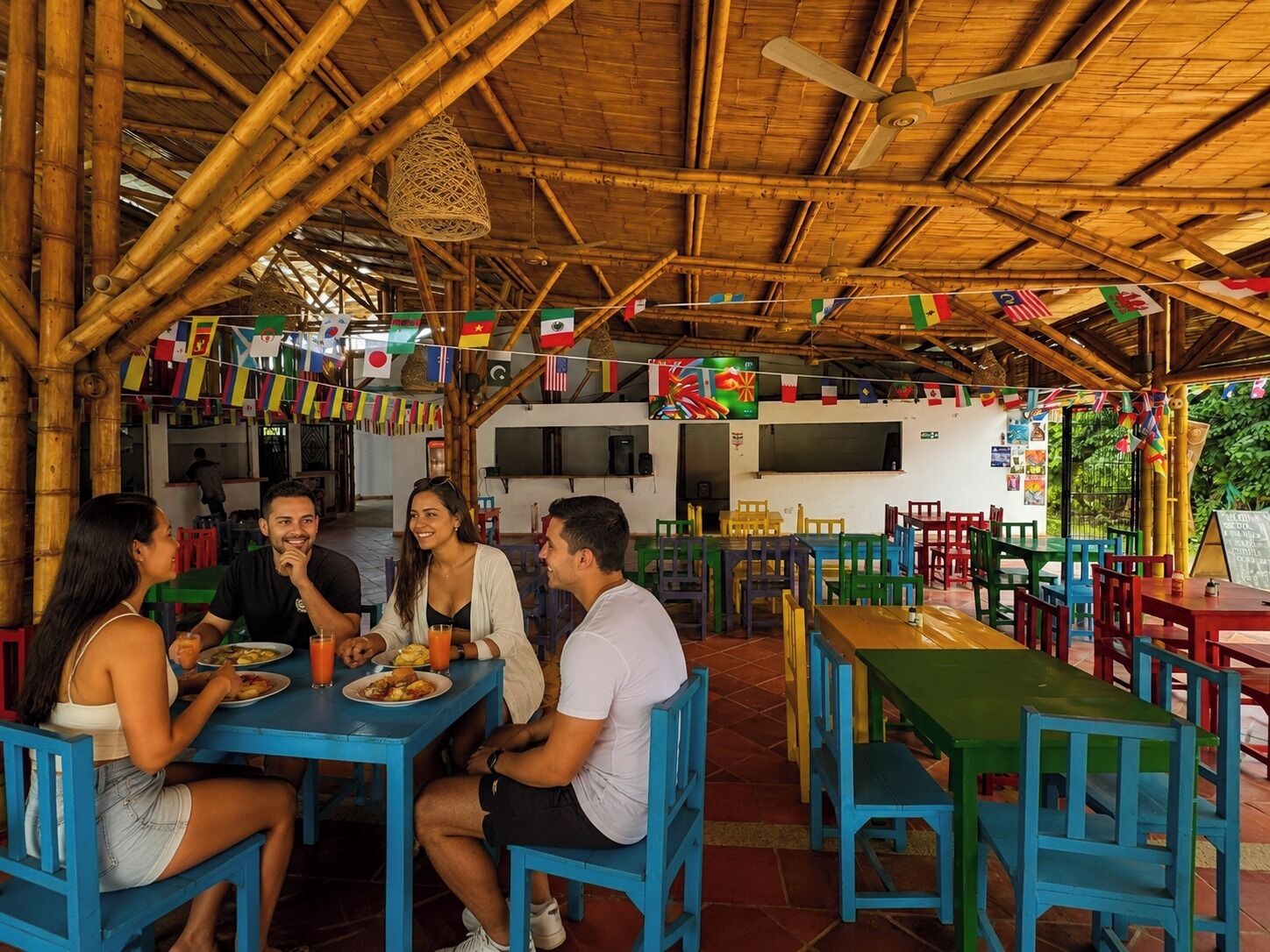 A restaurant with a bamboo roof, colorful flags, and a casual dining area with blue and green chairs.