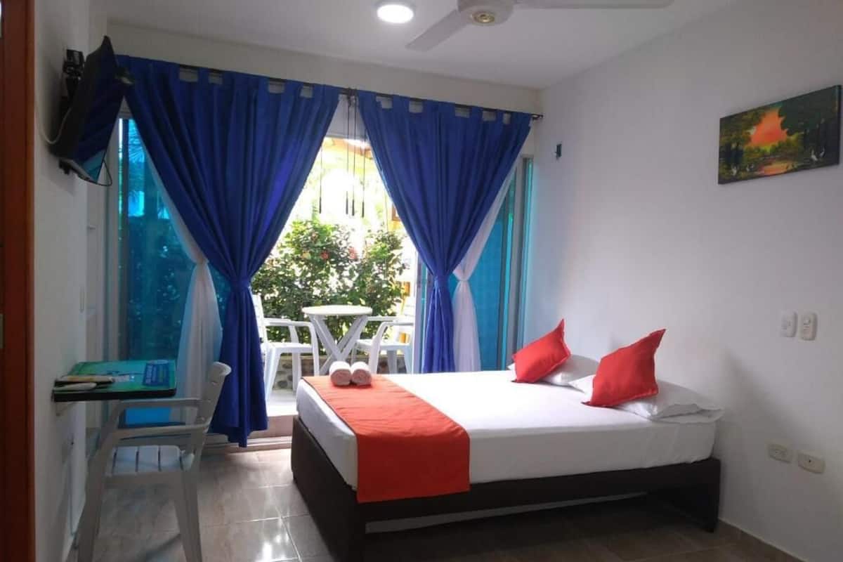 Un dormitorio con una cama, cortinas azules, una mesita con una silla y un cuadro en la pared.