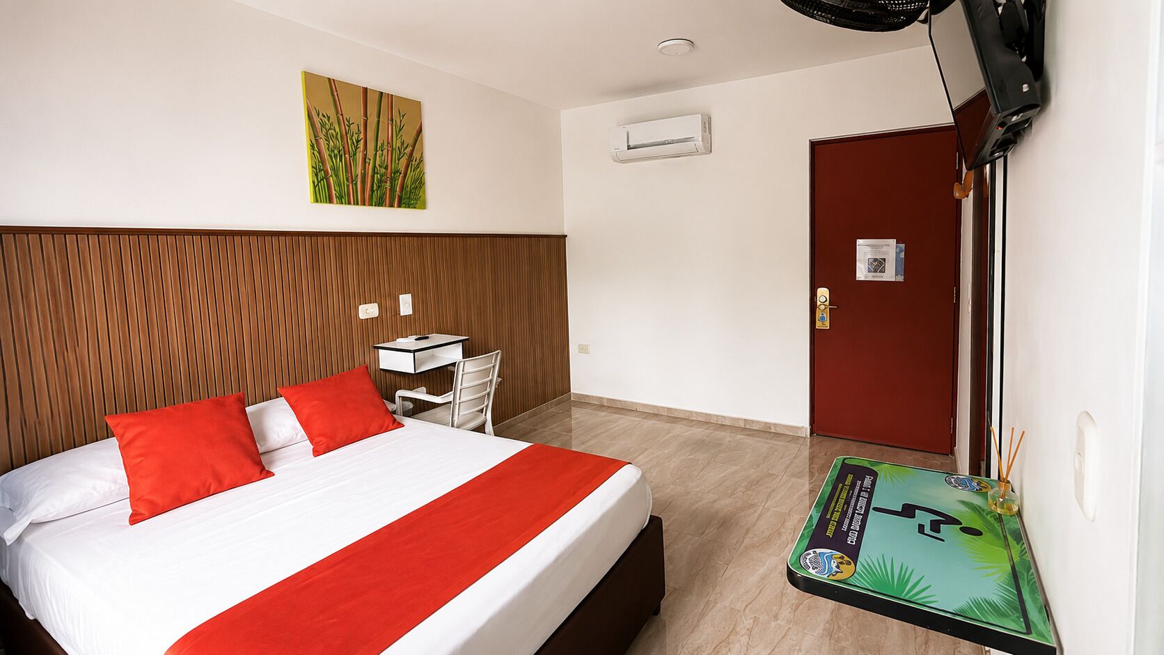 Ein Hotelzimmer mit Bett, Schreibtisch, Sessel, Fernseher und einer Tür.