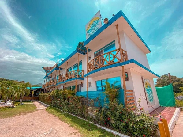 Un edificio de dos pisos con una decoración azul y blanca, un balcón en el piso superior y un letrero con un logotipo.