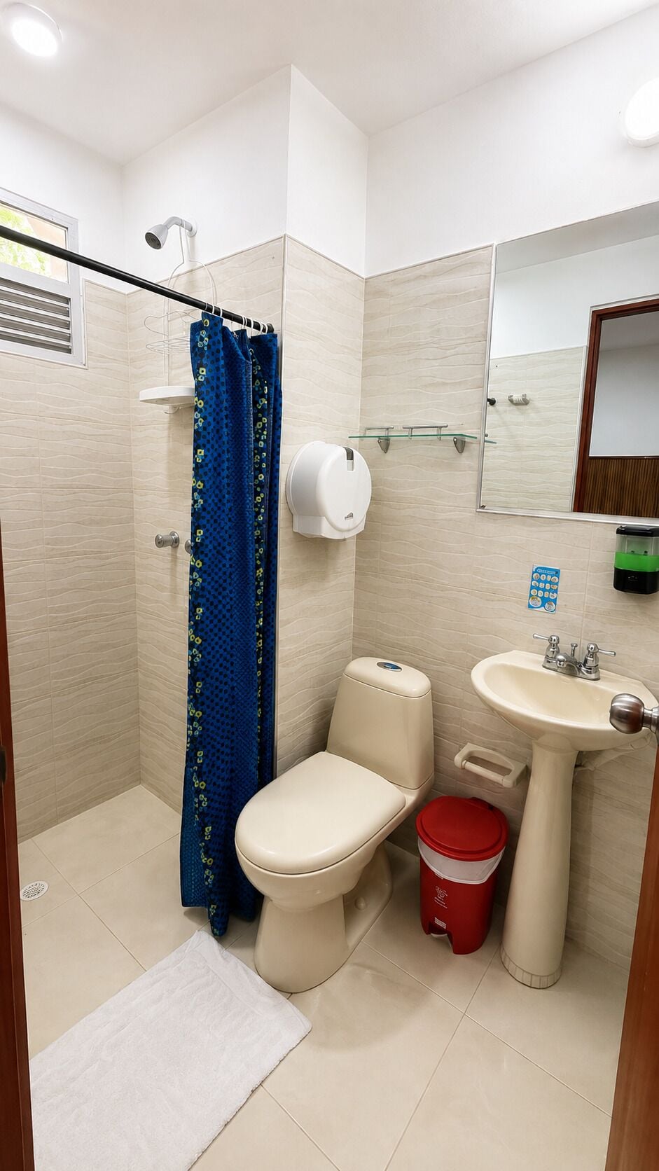 A bathroom with a toilet, shower, sink, and a mirror.