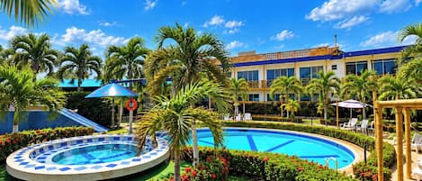 A hotel pool area with a circular pool, palm trees, and a building with a blue and white facade.