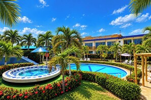A hotel pool area with a circular pool, palm trees, and a building with a blue and white facade. - La Rivera Playa Palomino (Dibulla)