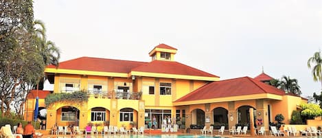 A large resort building with a swimming pool, multiple balconies, and outdoor seating areas.