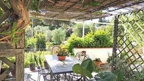 A covered patio with a table and chairs, surrounded by potted plants and a wooden trellis. - CASA CIRILLA - Casa Cirilla (Marciana)