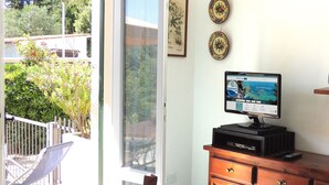 A room with a large window, a flat-screen TV on a wooden dresser, and two decorative plates on the wall. - CASA CIRILLA - Casa Cirilla (Marciana)