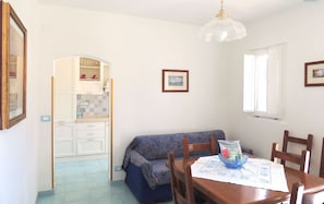 A dining area with a wooden table, chairs, a blue patterned sofa, and a hanging light fixture.