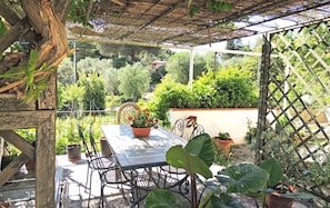 A covered patio with a table and chairs, surrounded by potted plants and a wooden trellis.
