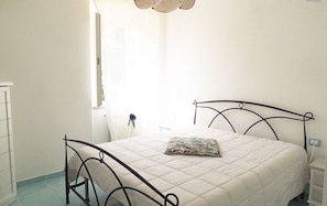 A bedroom with a bed, a window with curtains, and a bedside table.