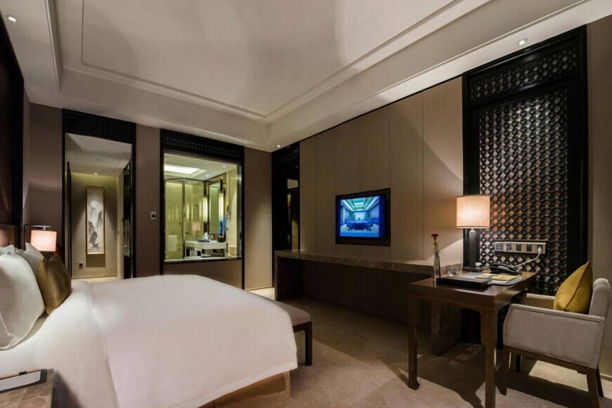 Habitación de hotel con una cama grande, un escritorio con silla, un televisor y un espejo.