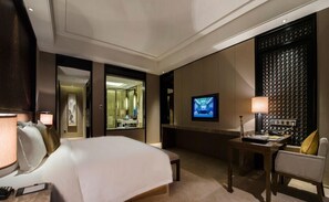 Quarto de hotel com uma cama grande, uma escrivaninha com cadeira, televisão e espelho.
