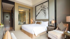 A hotel room with a large bed, a sitting area with a chair, a bedside table, and a large mirror. - Winlong International Hotel (Quanzhou)
