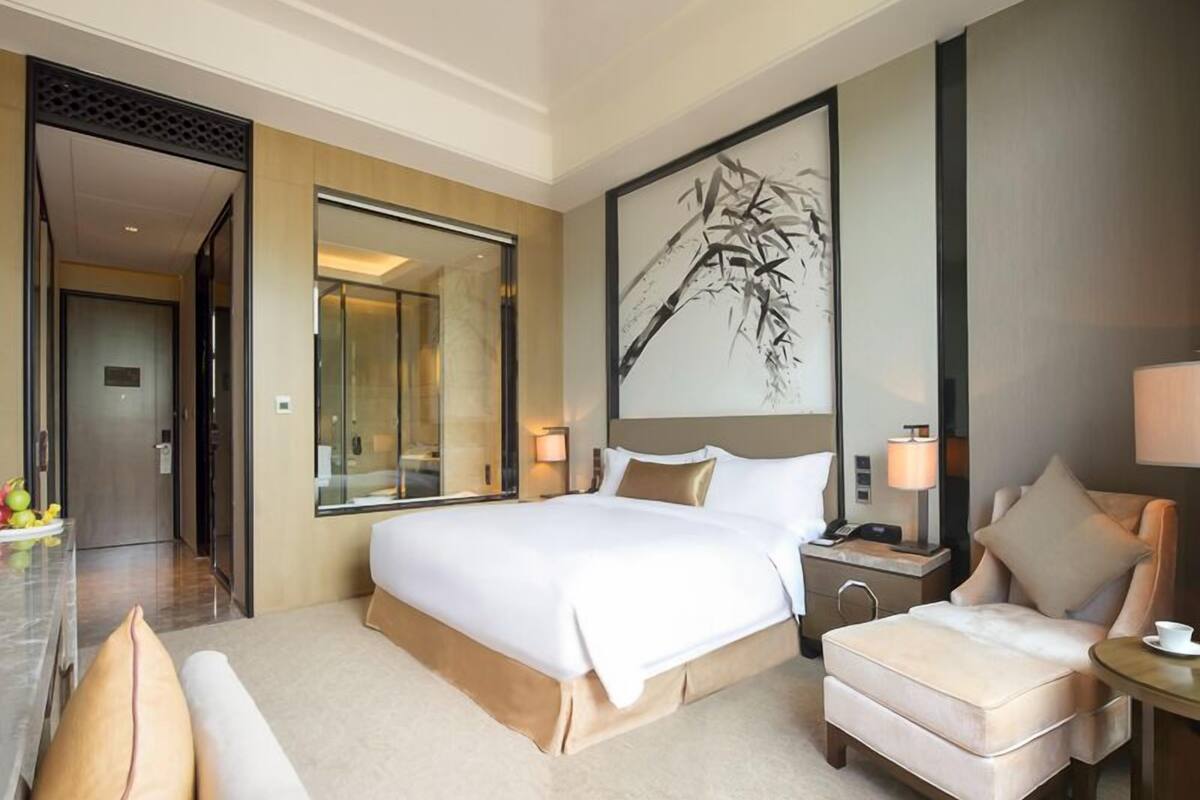 Habitación de hotel con una cama grande, un área de descanso con una silla, una mesita de noche y un espejo amplio.