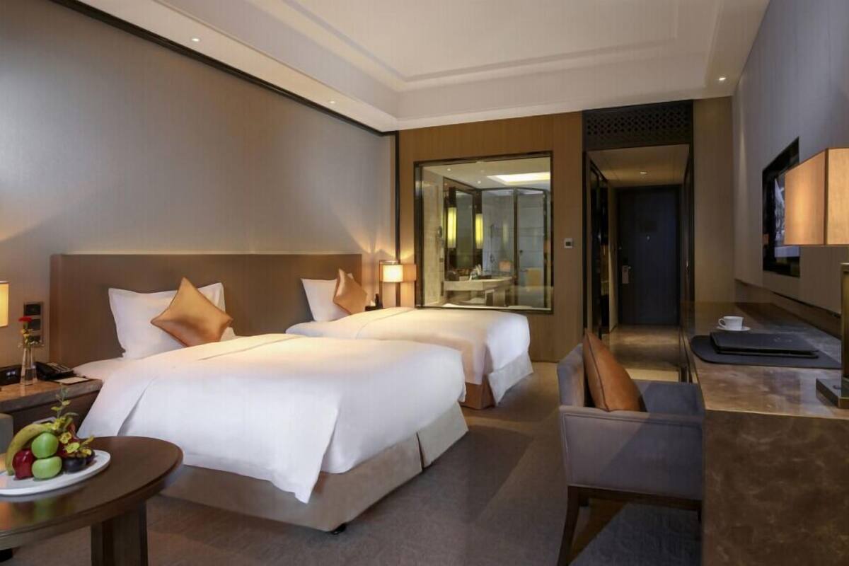 Habitación de hotel con dos camas, un escritorio con silla, un televisor y un espejo.