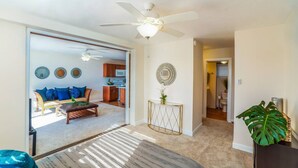 A spacious living area with a sofa, coffee table, and a ceiling fan. A kitchen is visible in the background.