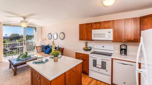 A modern kitchen with wooden cabinets, a white refrigerator, and a microwave. There is a dining area with a bench and a view of the outdoors.