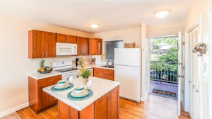 A compact kitchen with wooden cabinets, a white refrigerator, and a small island with dishes.