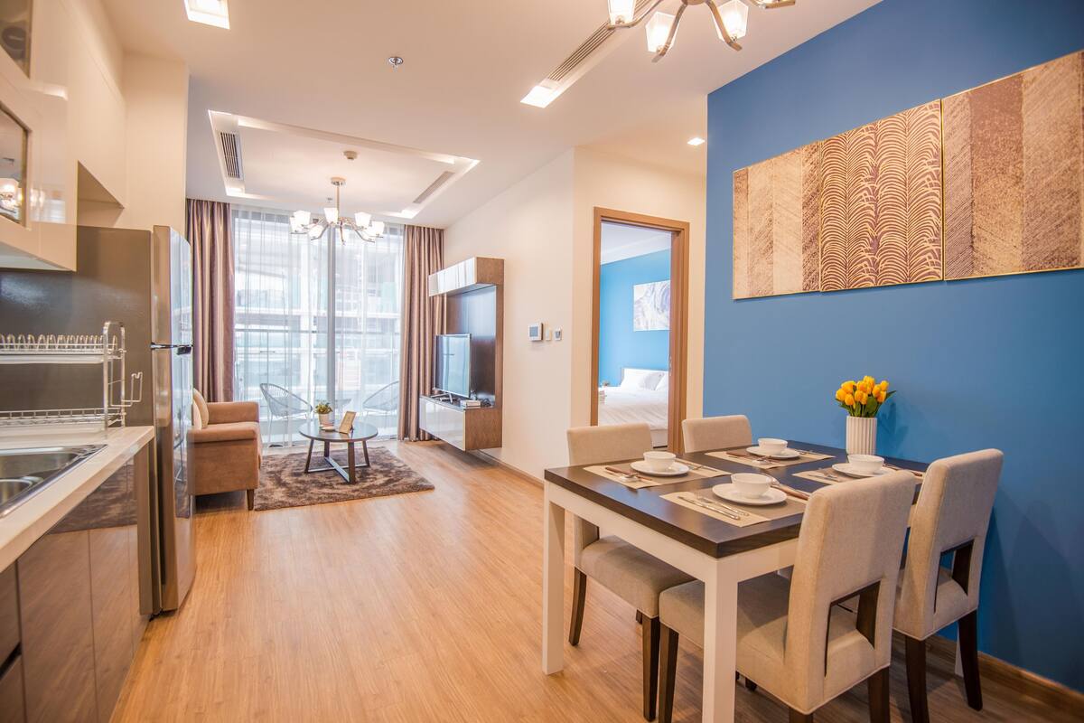 A modern hotel room with a kitchen, dining area, and a large window.