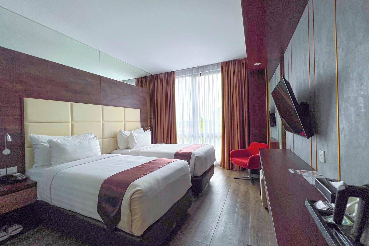 Habitació d'hotel amb dos llits, un escriptori, una televisió i una cadira vermella.
