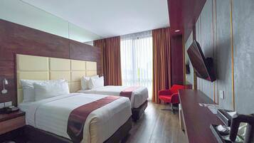 Een hotelkamer met twee bedden, een bureau, een televisie en een rode stoel.