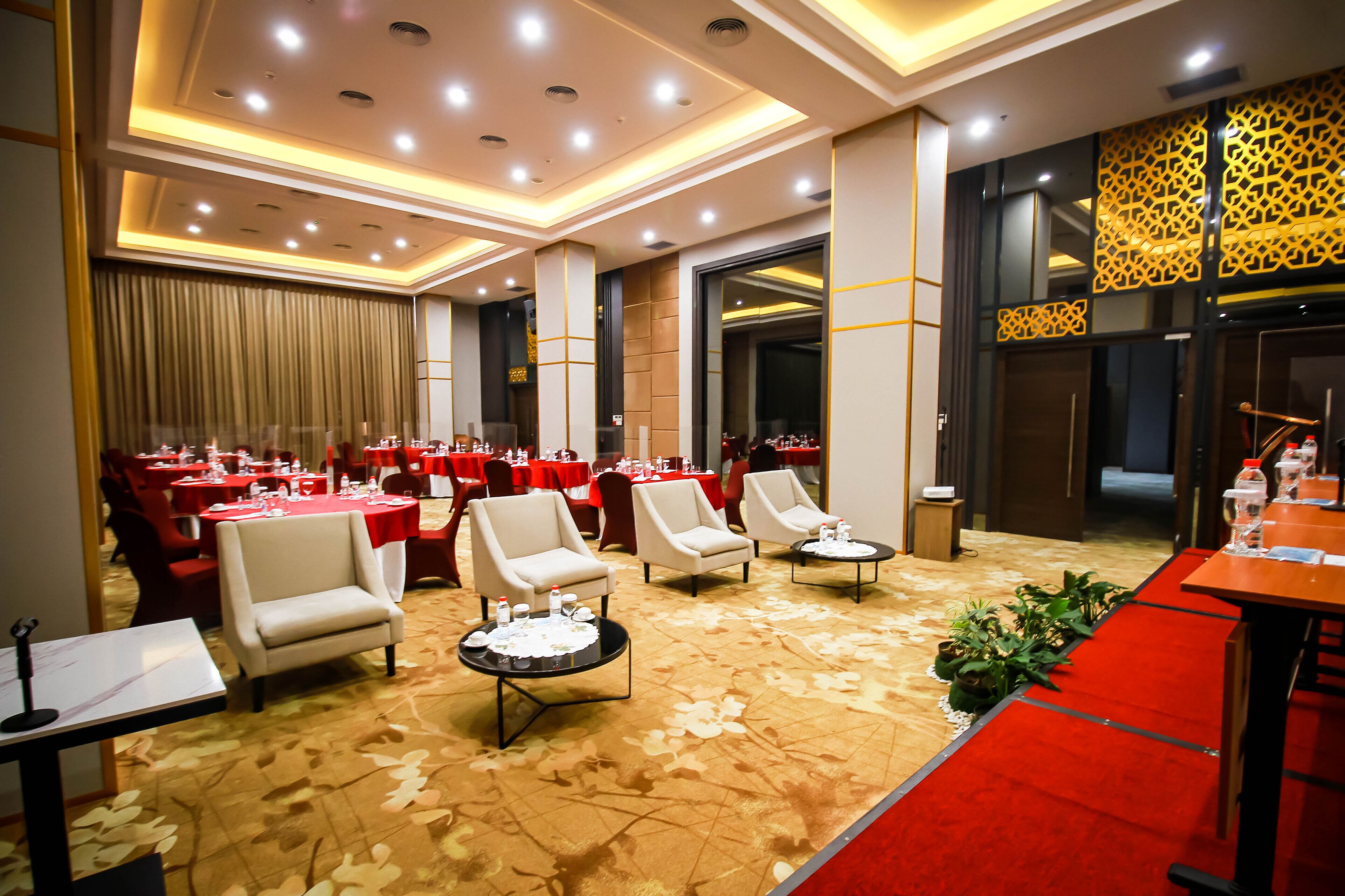 A banquet hall with round tables, chairs, and a red carpet.