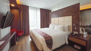 A hotel room with a large bed, a desk with a chair, a TV, and a bedside table with a lamp.