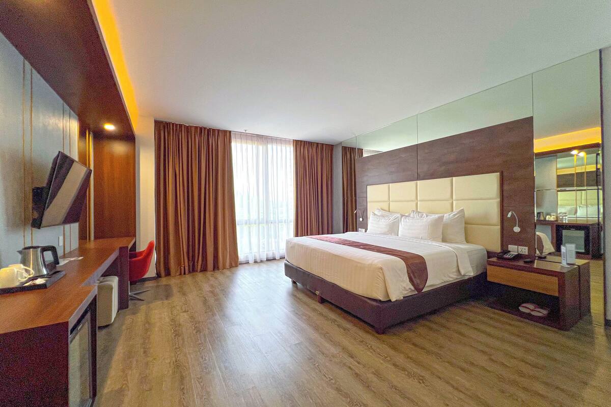 Una habitació d'hotel amb un llit gran, una taula de treball amb una cadira, una televisió i un mirall.