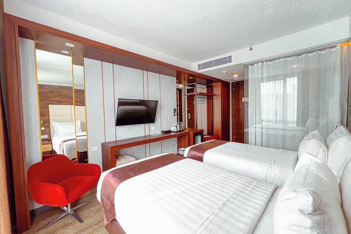 Habitació d'hotel amb dos llits, televisió, escriptori i una cadira vermella.