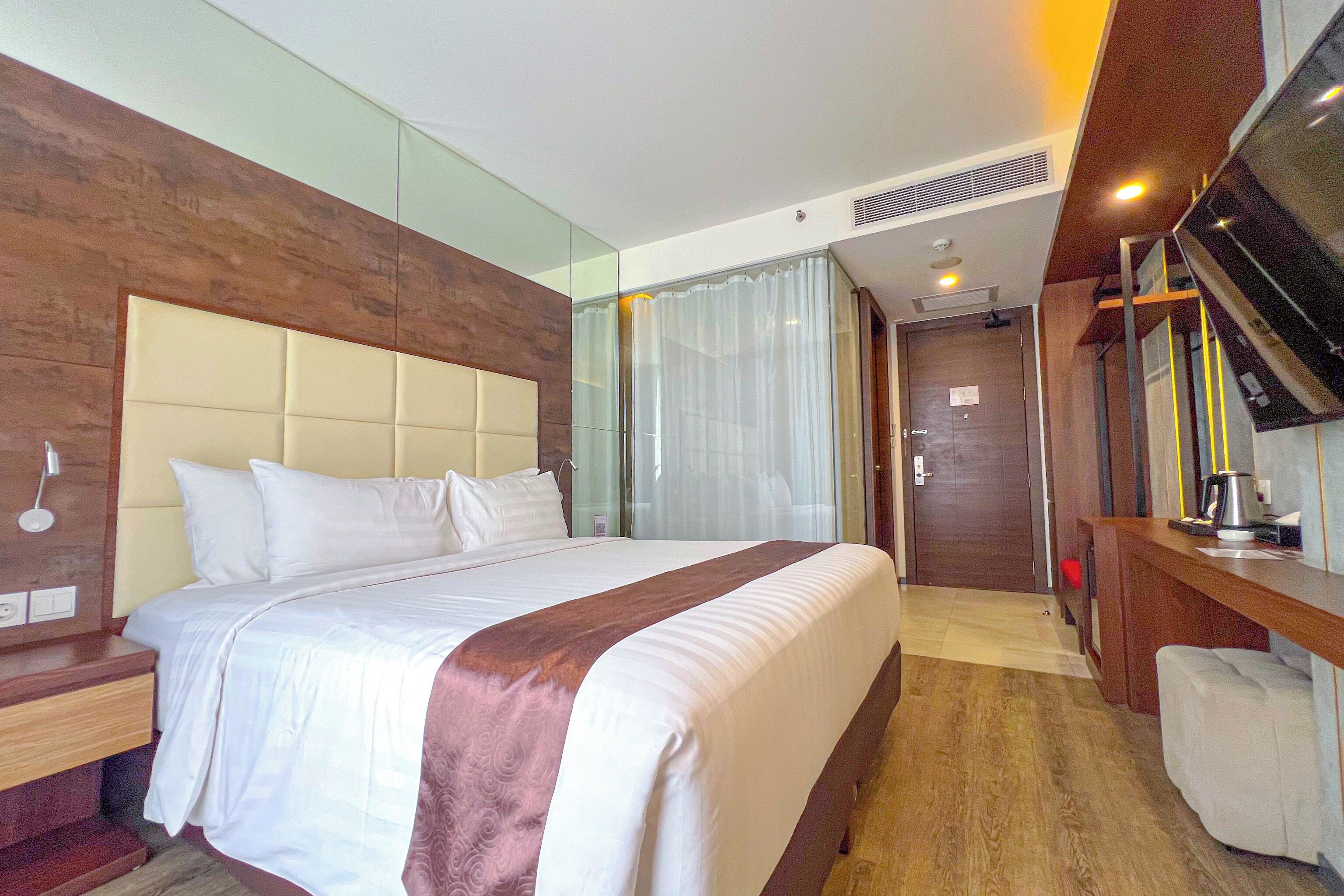 Una habitación de hotel con una cama grande, cabecera de madera, un escritorio con silla y un televisor.