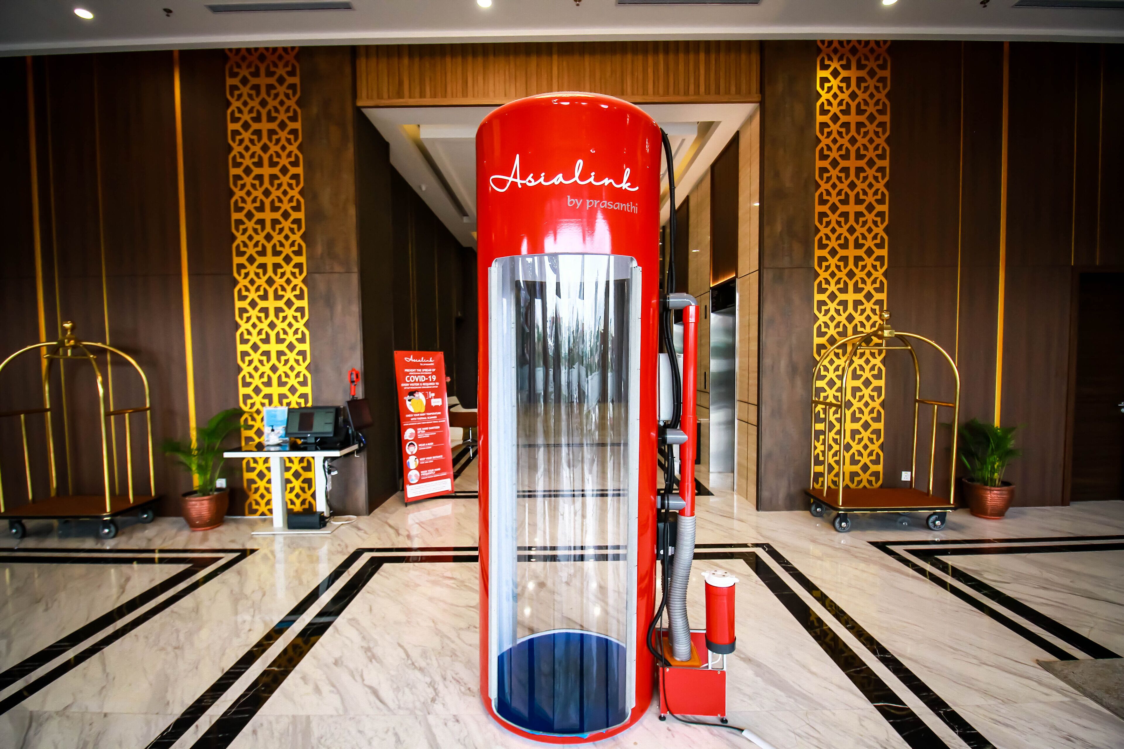 Un vestíbulo de hotel con un quiosco rojo de autoservicio, una recepción y un diseño de pared con motivos.