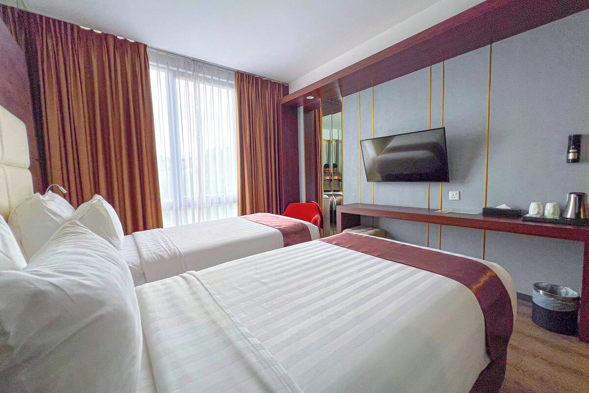 Habitació d'hotel amb dos llits, televisió, escriptori i mirall.