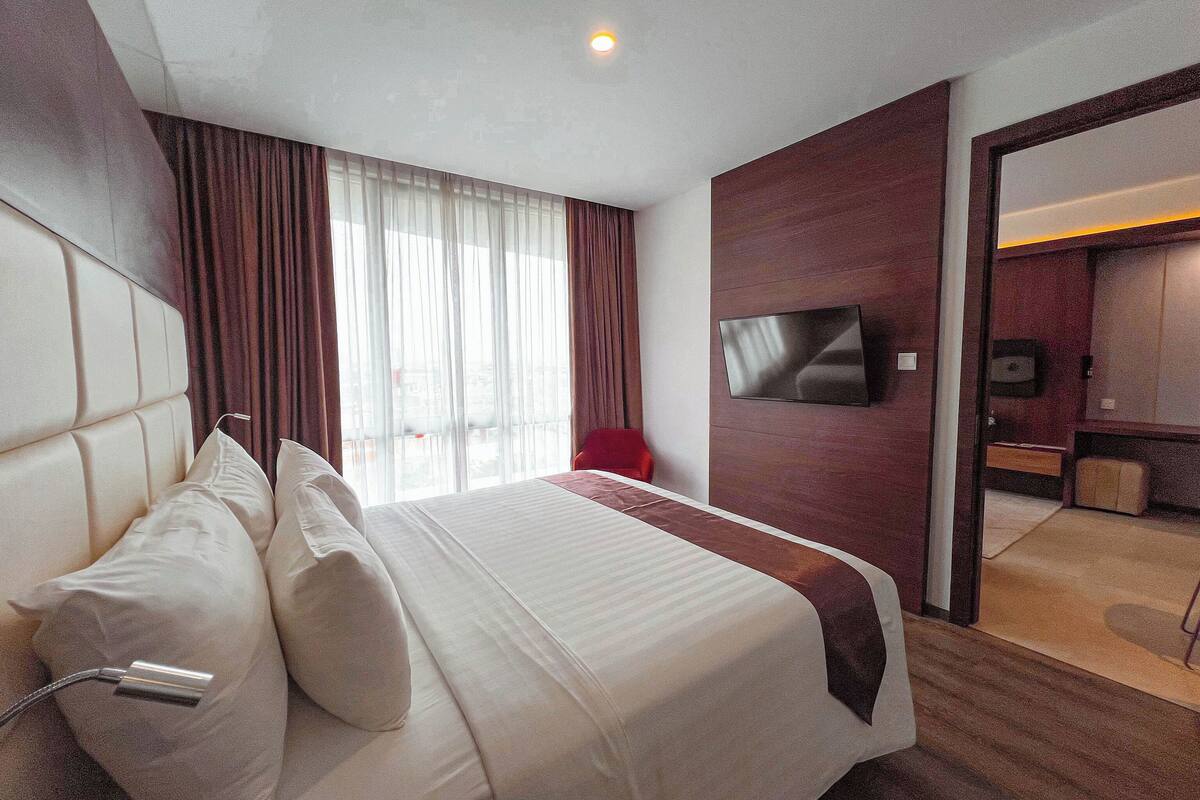 Una habitació d'hotel amb un llit gran, una televisió penjada a la paret i vistes a la ciutat per la finestra.
