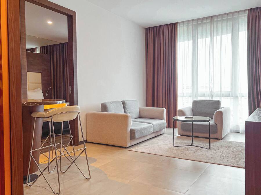 Een moderne woonkamer met een bank, twee fauteuils, een bijzettafeltje en een barkruk.