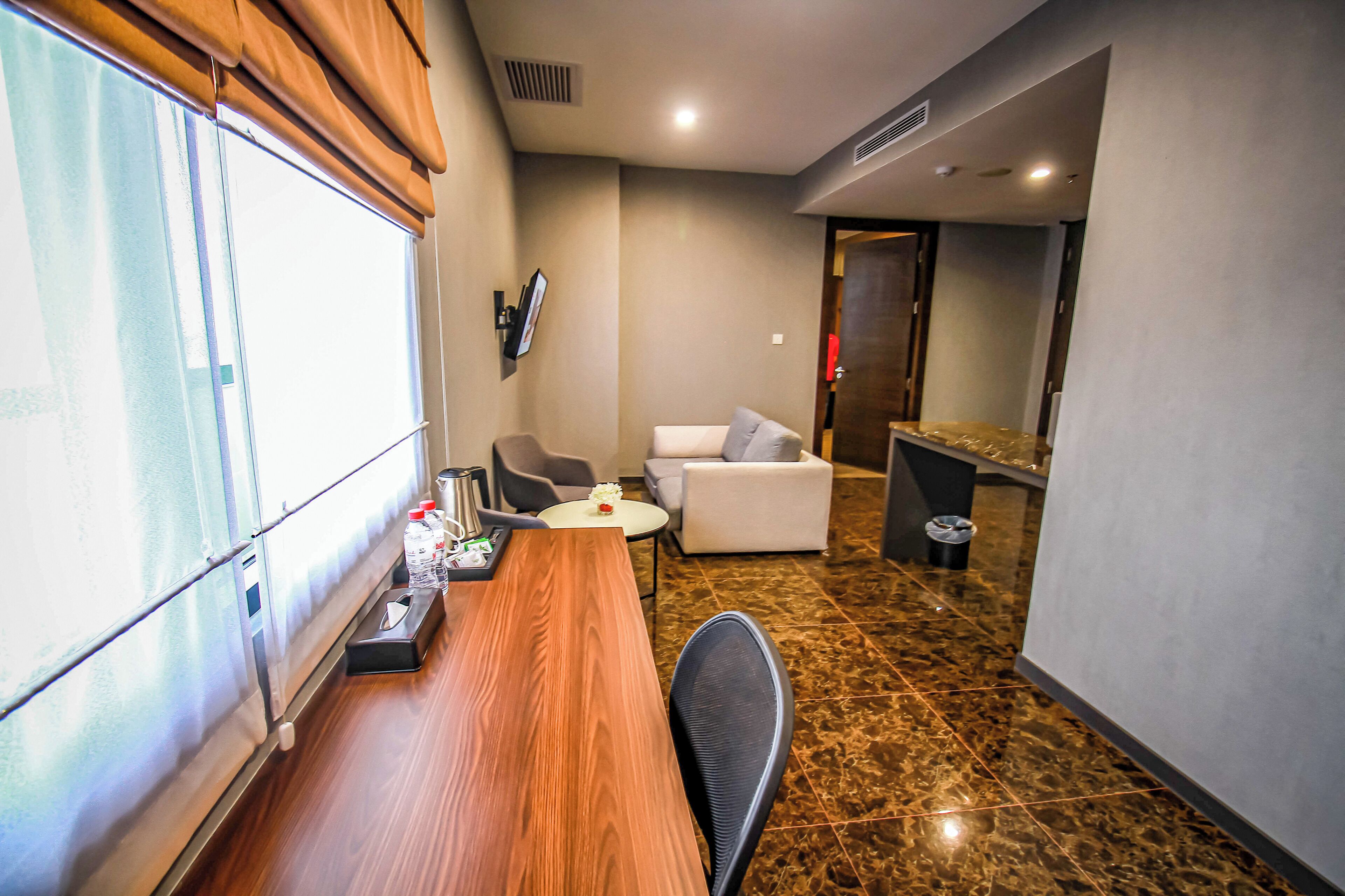 Una habitación de hotel con una mesa de comedor de madera, un sofá, una pequeña mesa redonda con un florero y un televisor montado en la pared.