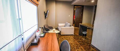 Una habitación de hotel con una mesa de comedor de madera, un sofá, una pequeña mesa redonda con un florero y un televisor montado en la pared.