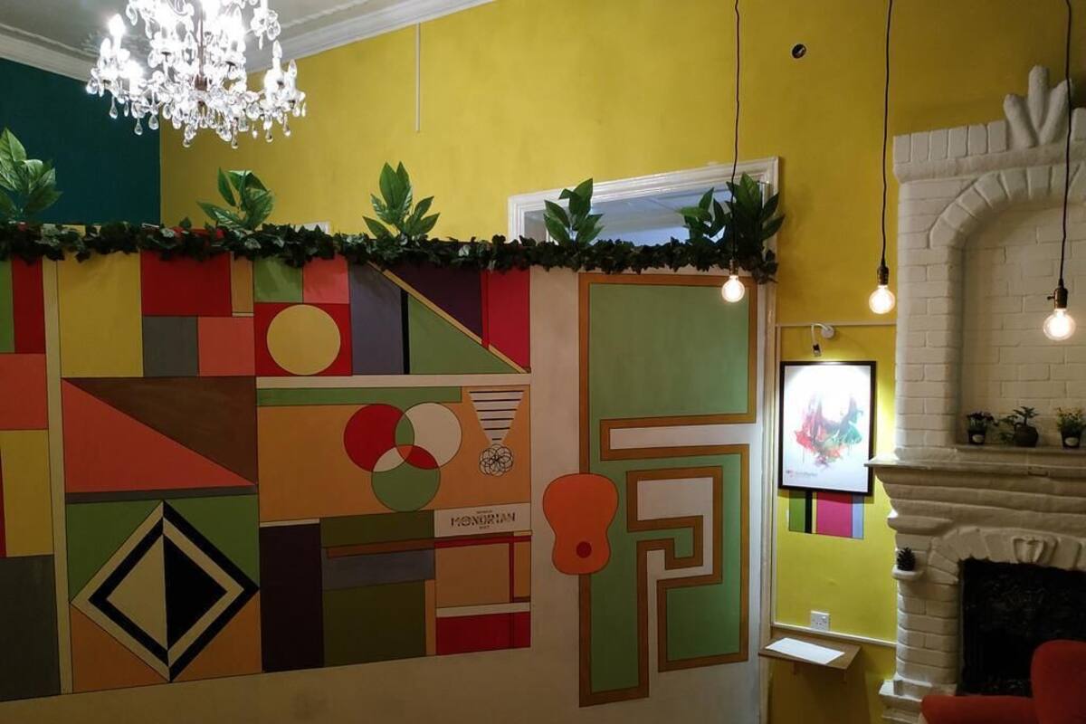 A room with a colorful geometric wall design, a chandelier, a fireplace, and a red armchair.