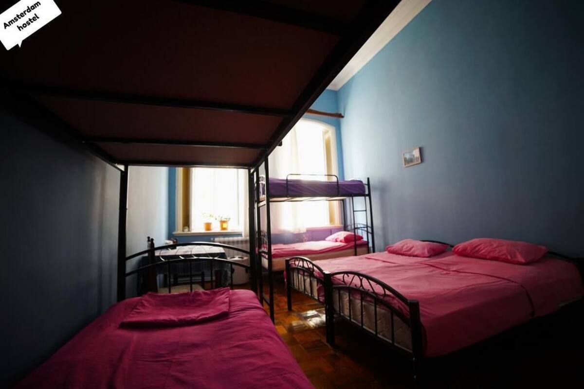 A dormitory room with bunk beds, a small table, and a window with natural light.