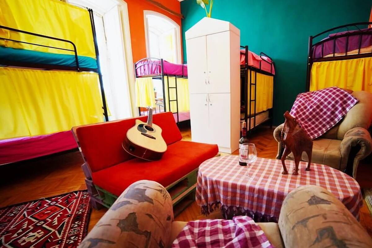 A colorful room with bunk beds, a red sofa, a guitar, a small table with a wine glass, and a dog.