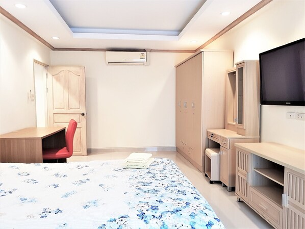 Un dormitorio con cama, escritorio, silla, armario, televisor y aire acondicionado.