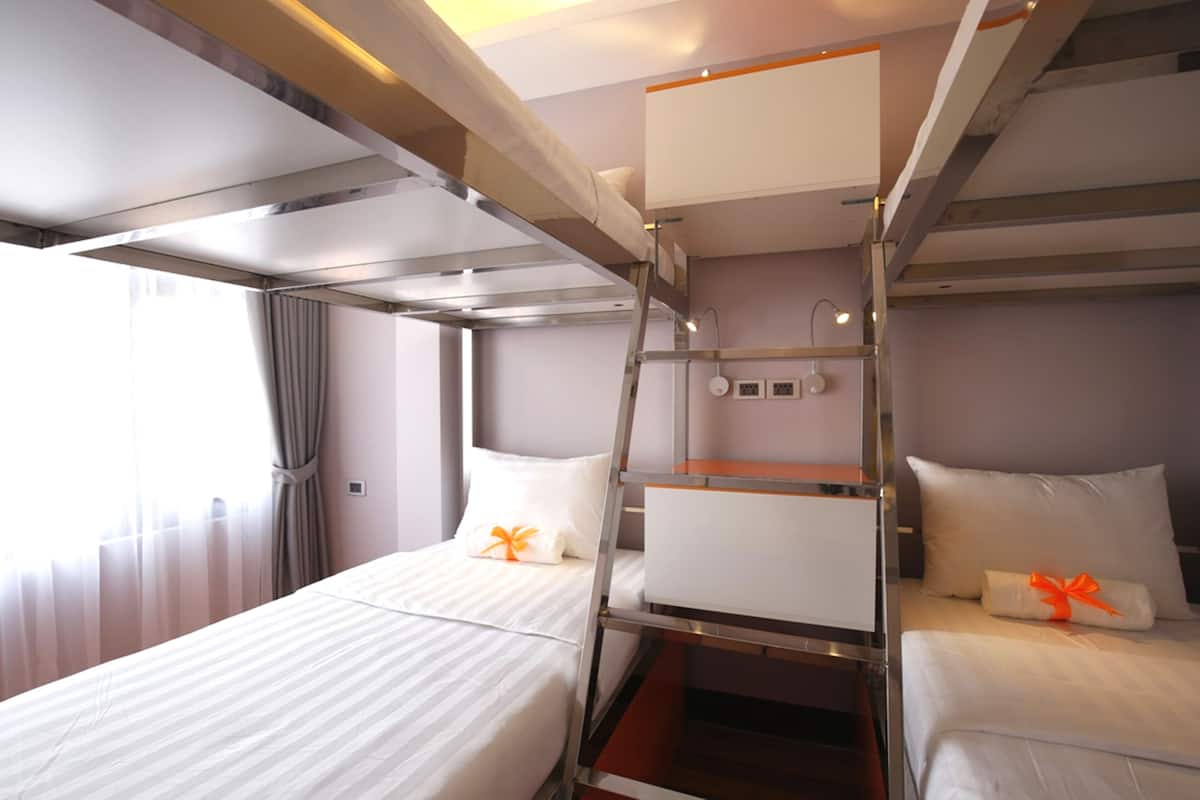 A hotel room with bunk beds, a window with curtains, and a bedside table.