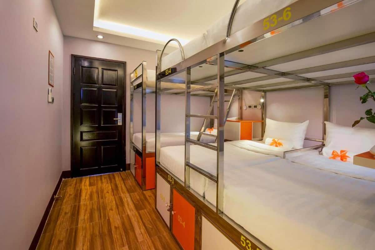 A hotel room with bunk beds, a wooden floor, and a door.