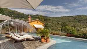 A pool area with lounge chairs, a glass-enclosed structure, and a view of a mountain. - Villa La Massa - Exclusive Use - Heated Pool (Castel San Niccolo  -  Arezzo)