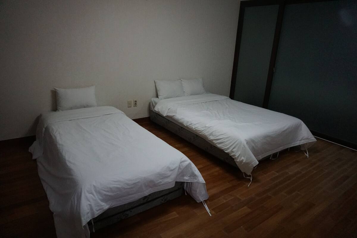 Deux lits simples avec du linge de lit blanc, dans une pièce dotée d’un plancher en bois et d’une porte coulissante de couleur foncée.