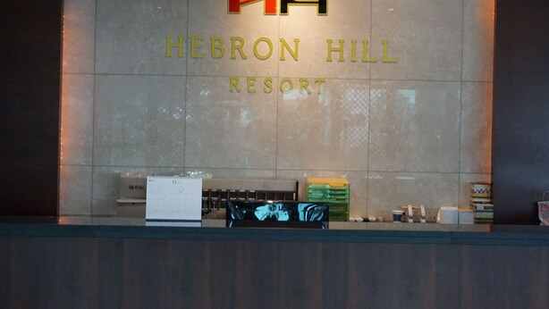 En receptionsdisk på Hebron Hill Resort, med en logotyp ovanför namnet, en kalender och några föremål på disken.