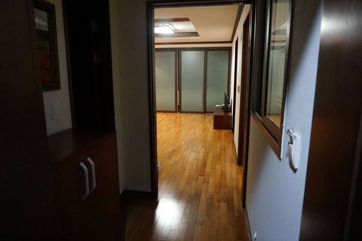 Un couloir au plancher de bois menant à une pièce dotée d’une porte coulissante et d’une petite table.