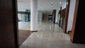 En rymlig hall med ett polerat klinkergolv, stora vita pelare och glasdörrar som leder till ett annat område.