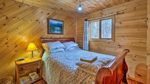 Een slaapkamer in een houten hutje, met een bed, nachtkastje, lamp en een raam met gordijnen.