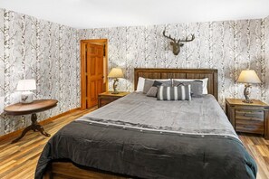A bedroom with a large bed, two bedside tables with lamps, a wooden door, and a deer head mounted on the wall.