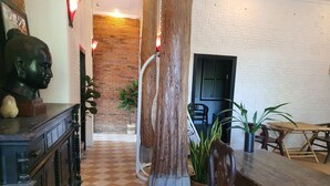 A dining area with a wooden table and chairs, a brick wall, and a large tree trunk in the center. - Brightness Villa (Battambang)